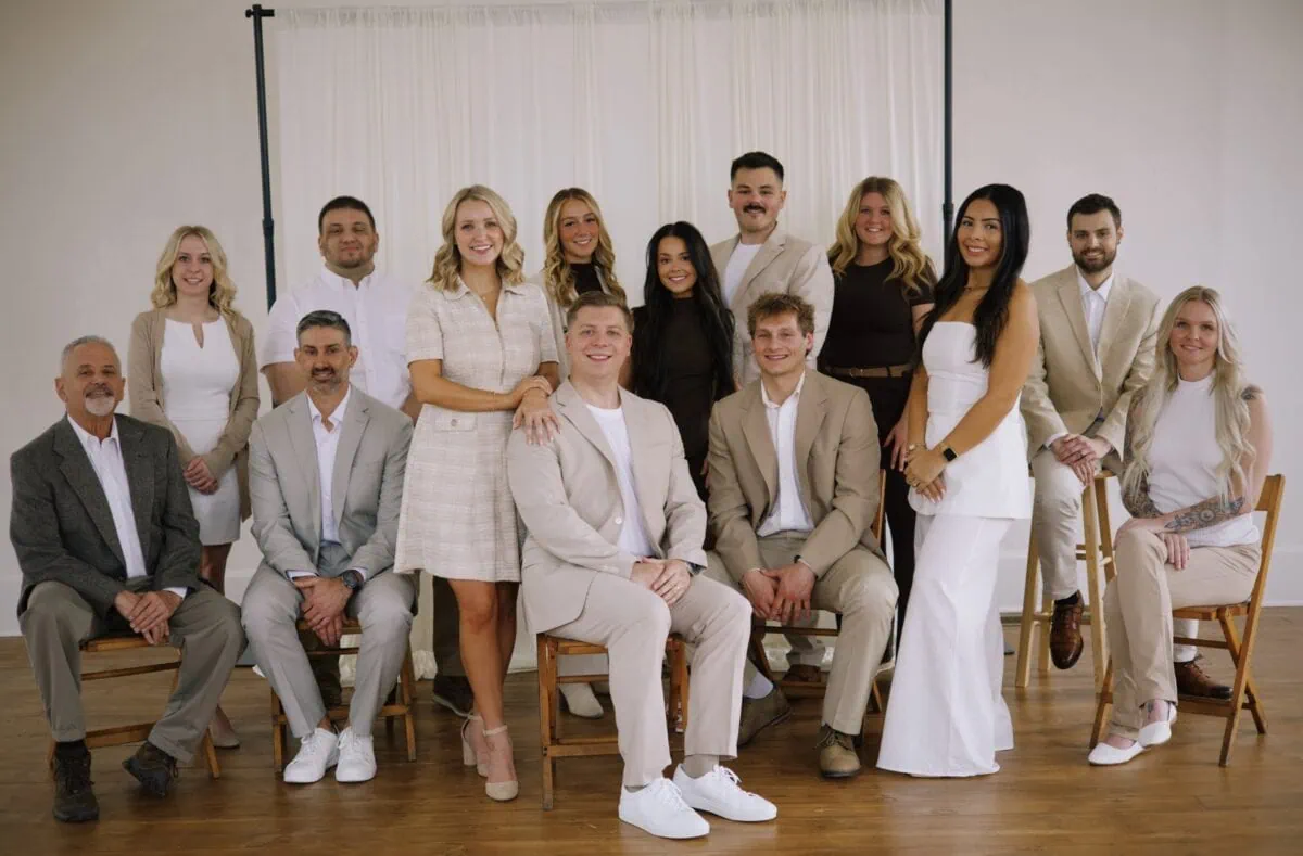 Fell Realty agents wearing neutral toned clothing posing together in a light airy room with a sheer white curtain backdrop.